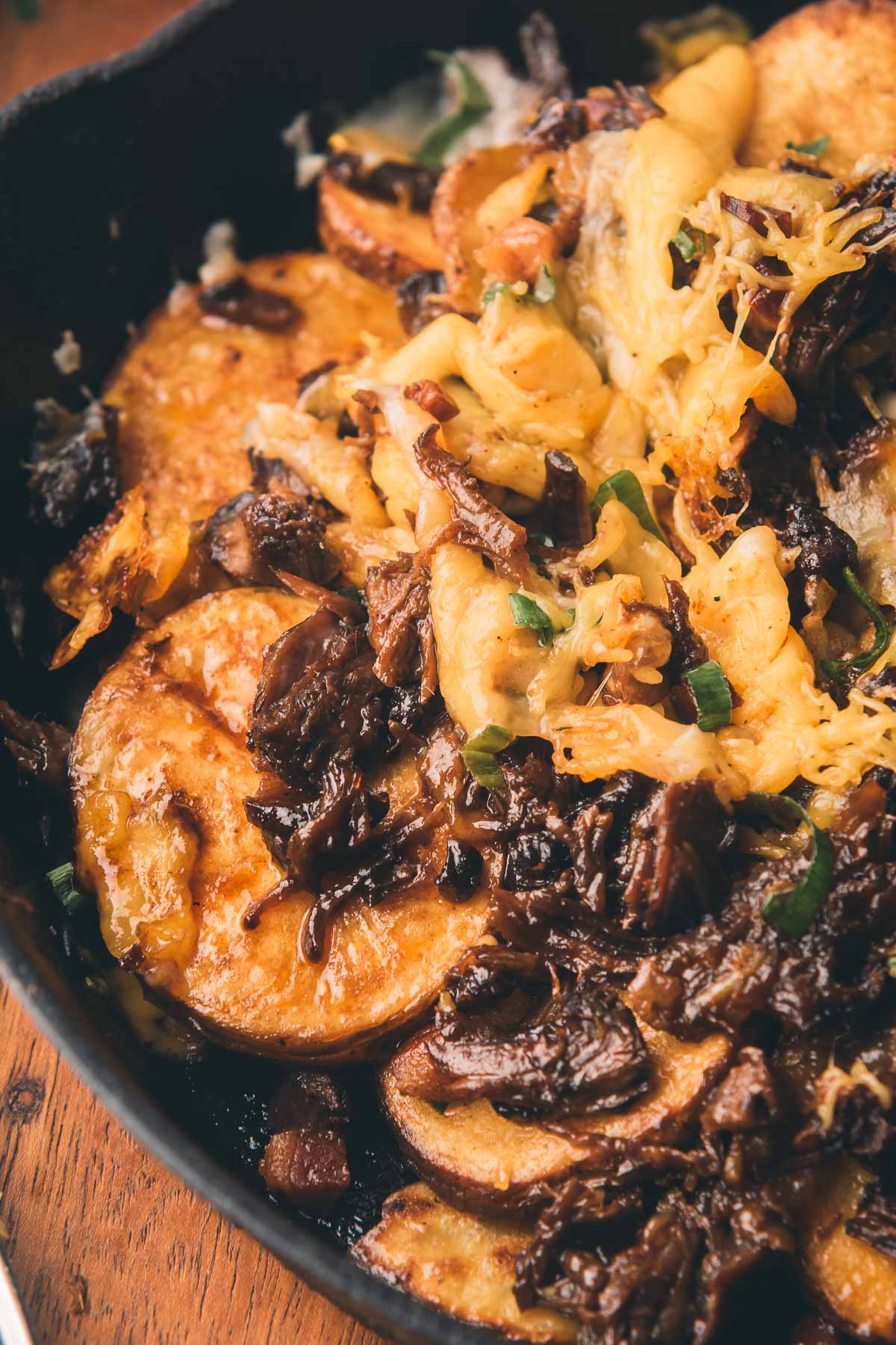 Sliced potatoes topped with shredded beef, melted cheese, and green onions in a cast iron skillet.