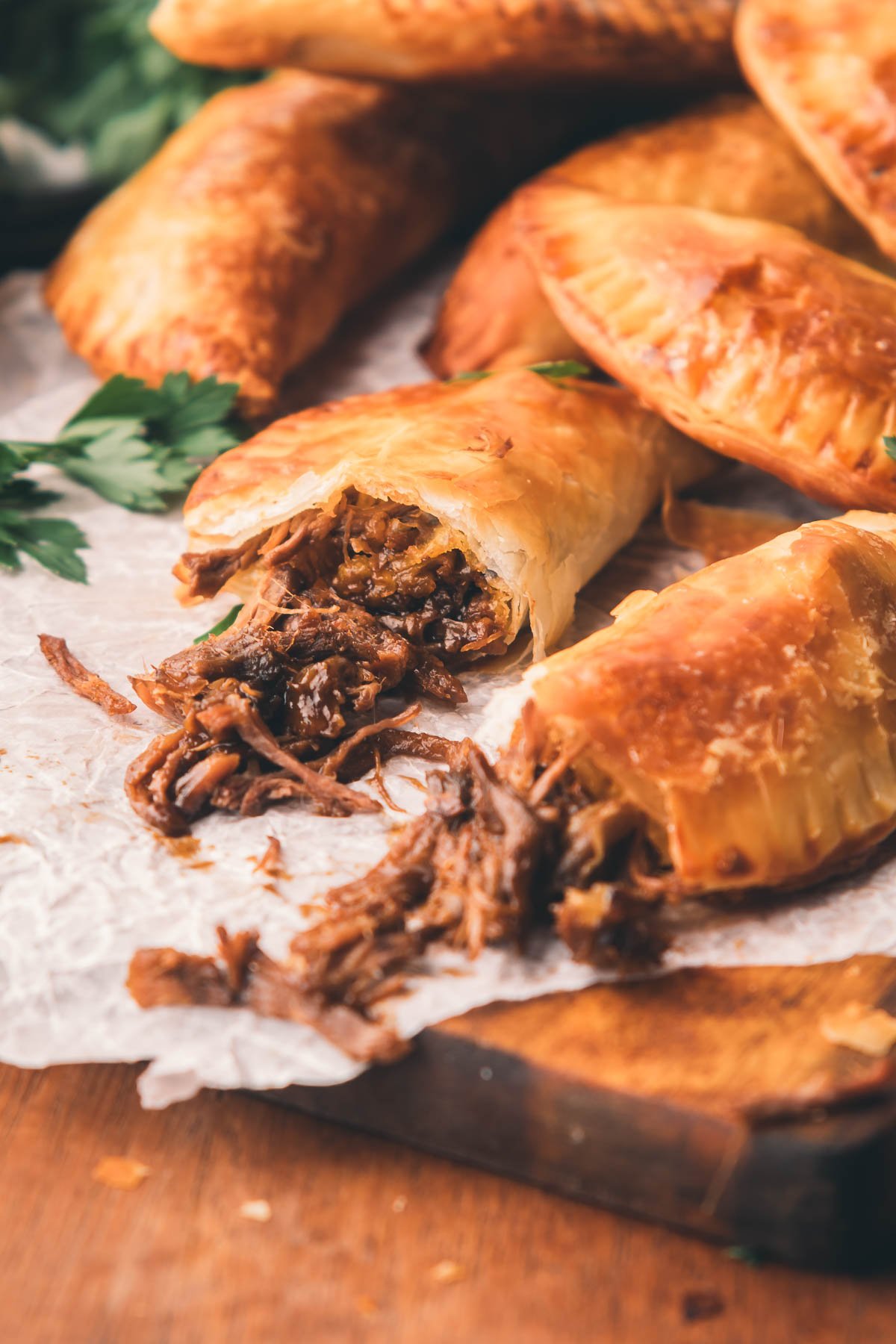 Close-up of hand pies opened on parchment paper, one split open to reveal shredded beef filling.