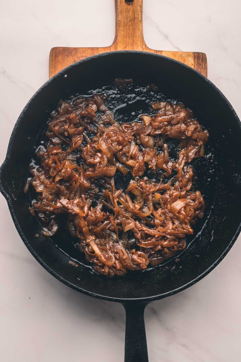 Caramelized onions in a black cast iron skillet on a wooden board, viewed from above.