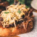An open-faced sandwich with leftover stout braised beef, melted cheese, and a garnish of parsley on toasted bread.