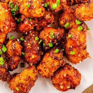 Close-up of sweet chili chicken bites garnished with chopped green onions and sesame seeds on a white plate.
