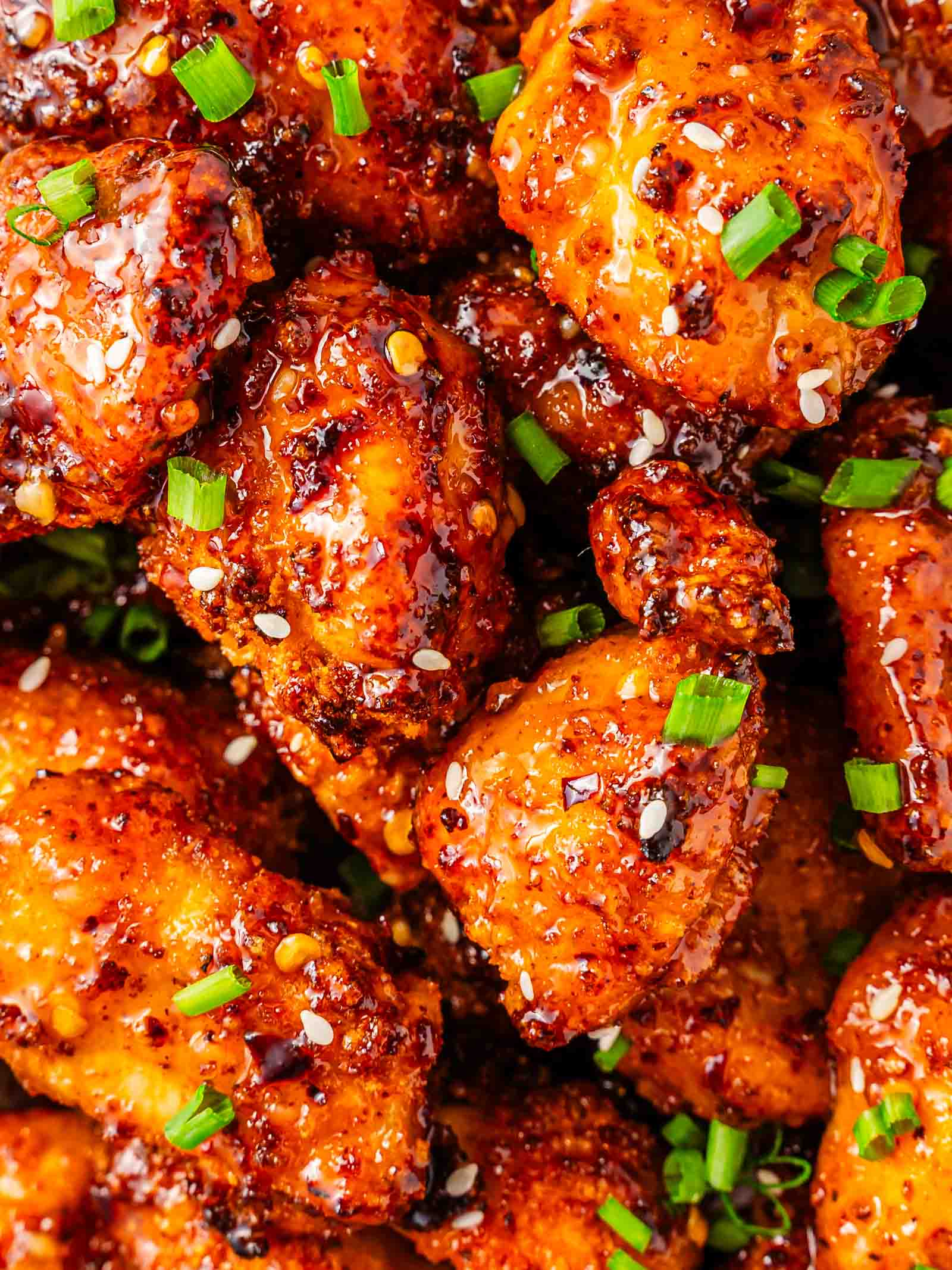 Close-up of sweet chili chicken bites garnished with chopped green onions, red pepper flakes, and sesame seeds.