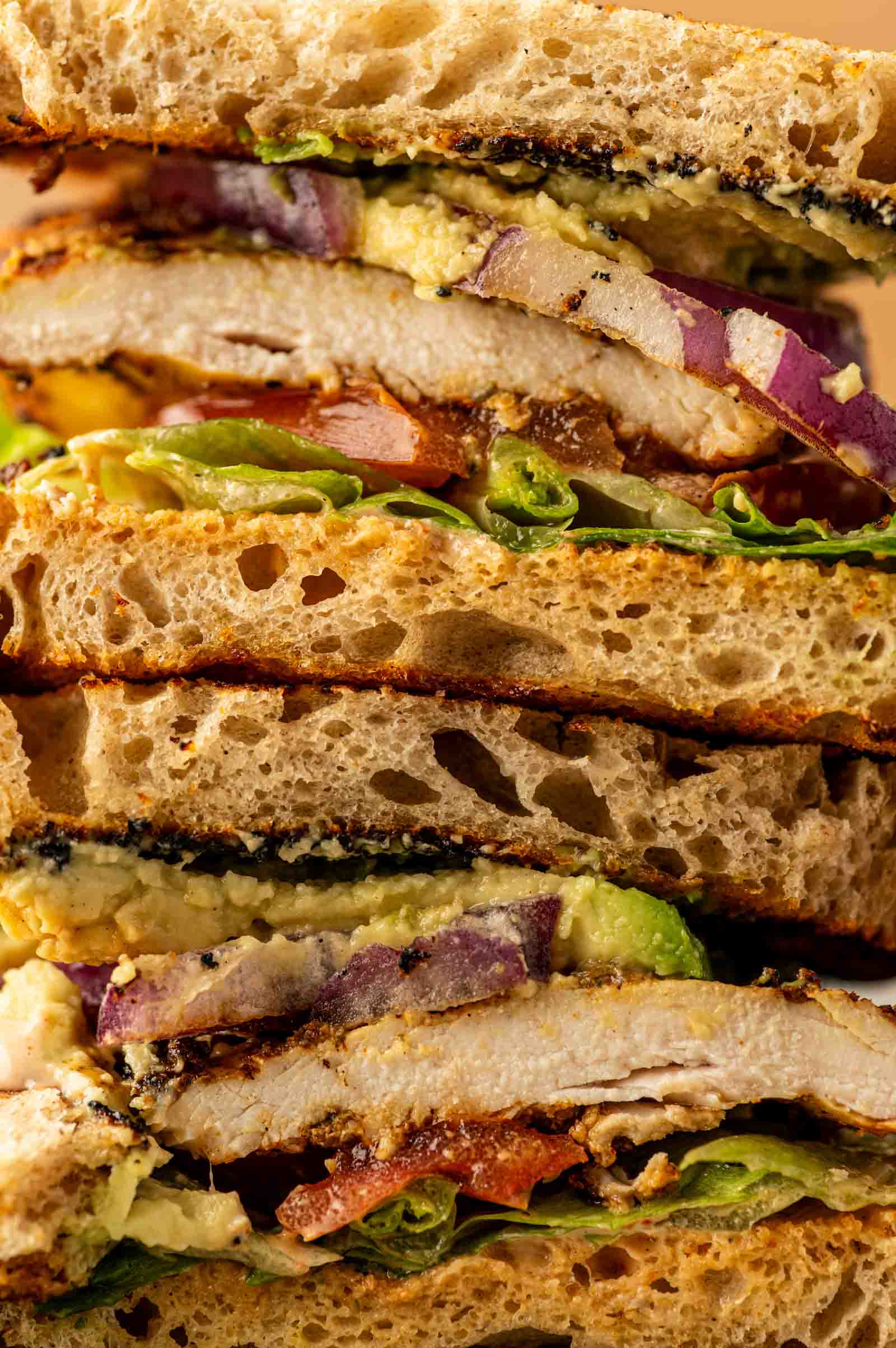 Close-up of stacked grilled chicken sandwiches with lettuce, red onion, and sauce between slices of toasted bread.