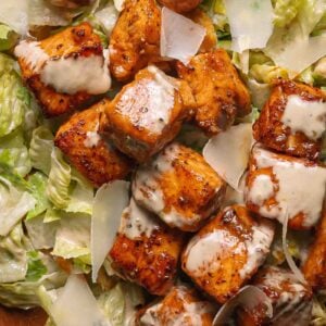 Hot honey salmon bites pieces with miso Caesar dressing and shaved parmesan on a bed of romaine lettuce.