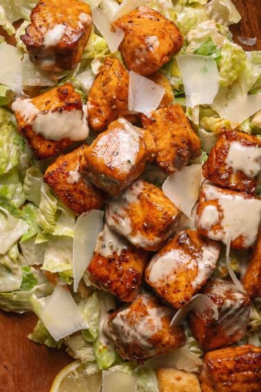 Hot honey salmon bites pieces with miso Caesar dressing and shaved parmesan on a bed of romaine lettuce.