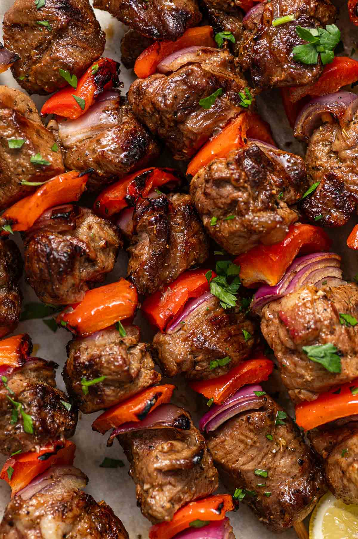 Grilled lamb skewers with red bell peppers and red onions, garnished with chopped herbs.