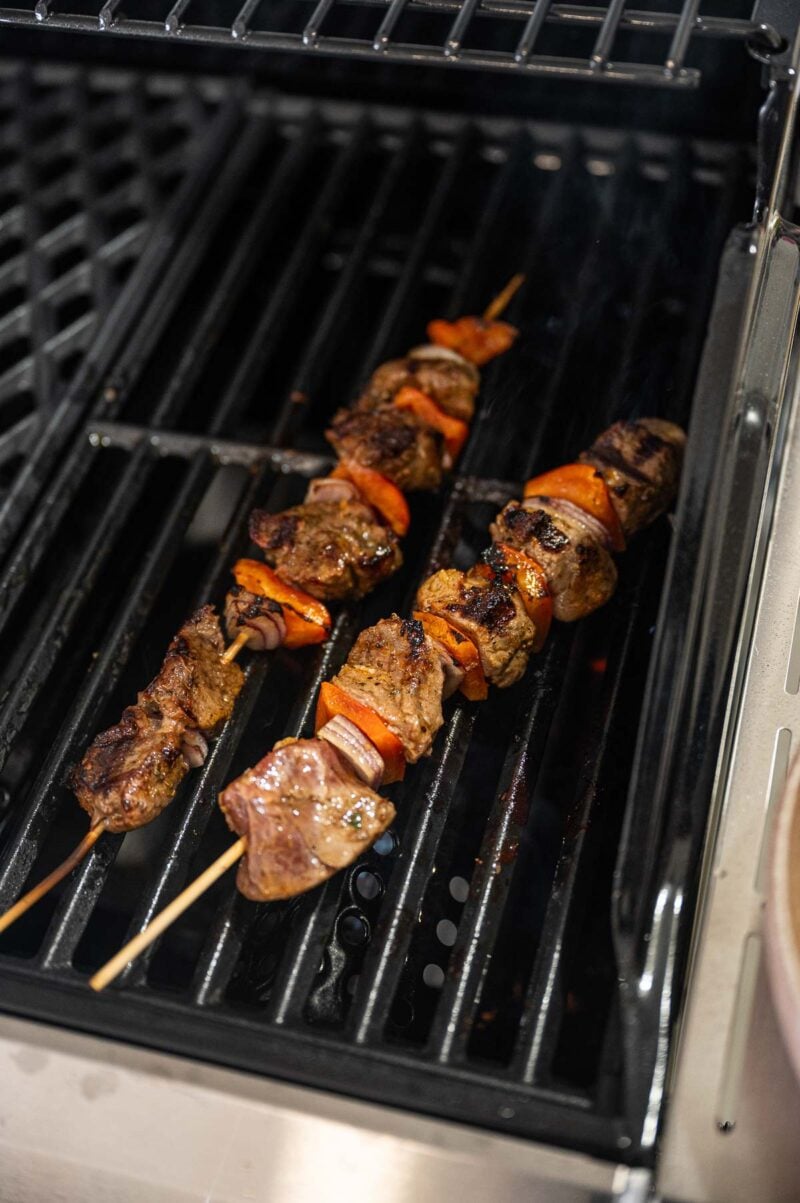 Two skewers of grilled lamb and vegetables are cooking on a grill.