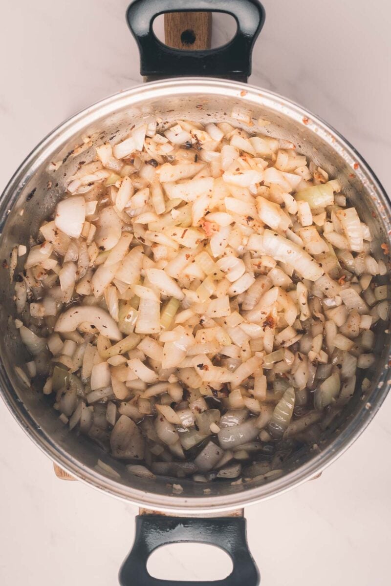 Chopped onions being sautéed in a stainless steel pot, viewed from above.