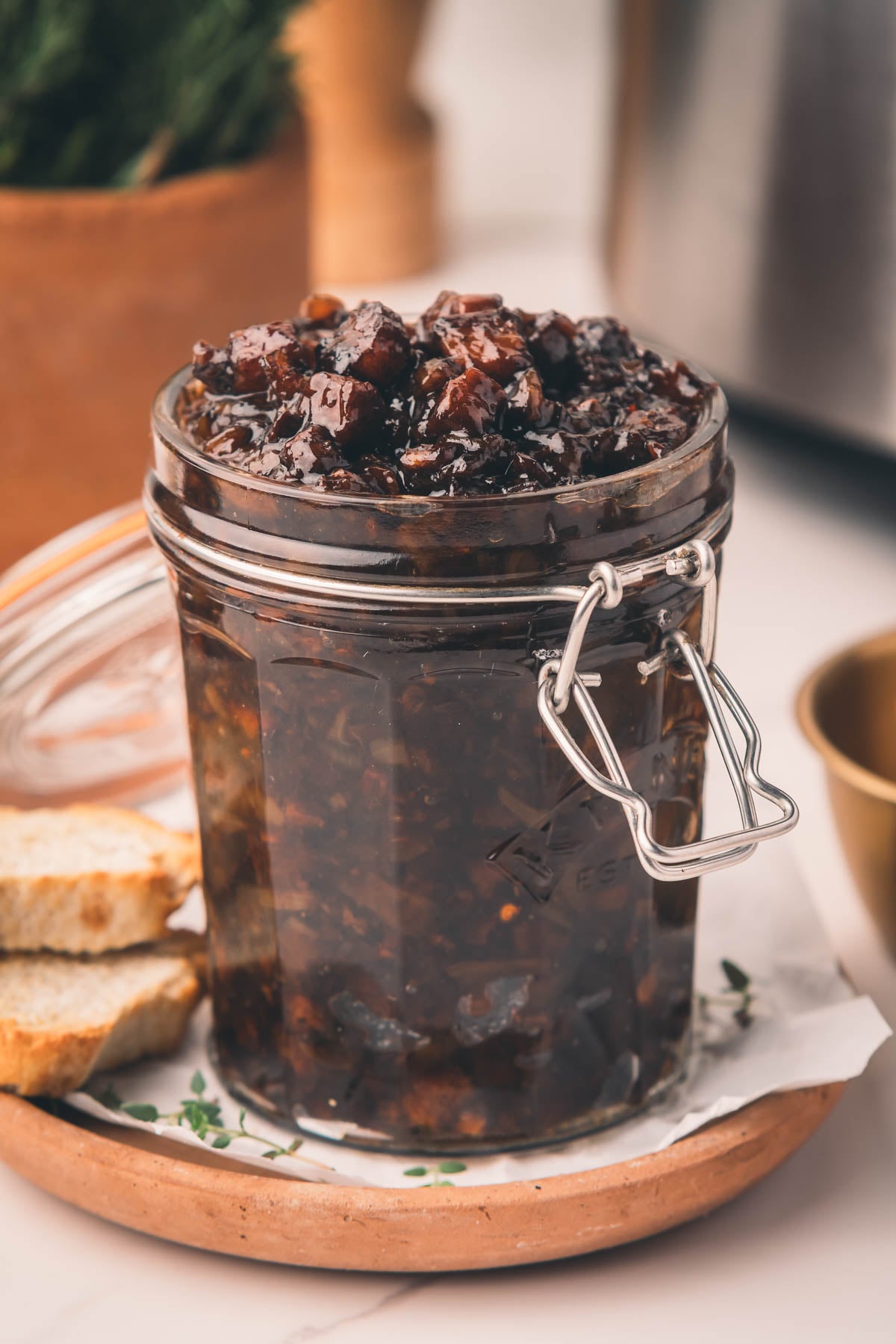 A glass jar filled with bacon jam sits on a plate with two slices of bread beside it.