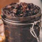 A glass jar filled with chunky, dark brown bacon jam, with a metal clasp lid, sits on a countertop.