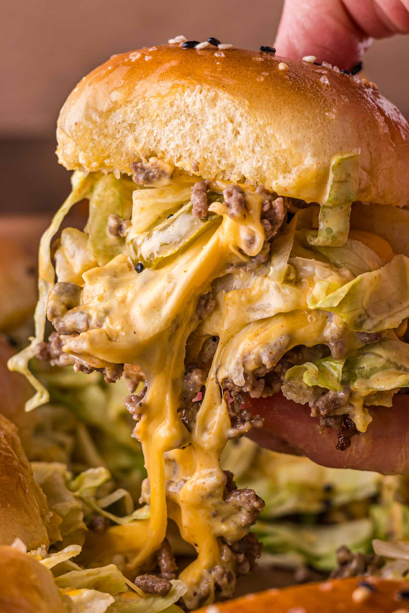 A close-up of a big mac slider with shredded lettuce, ground beef, and gooey melted cheese spilling out from a sesame seed bun.
