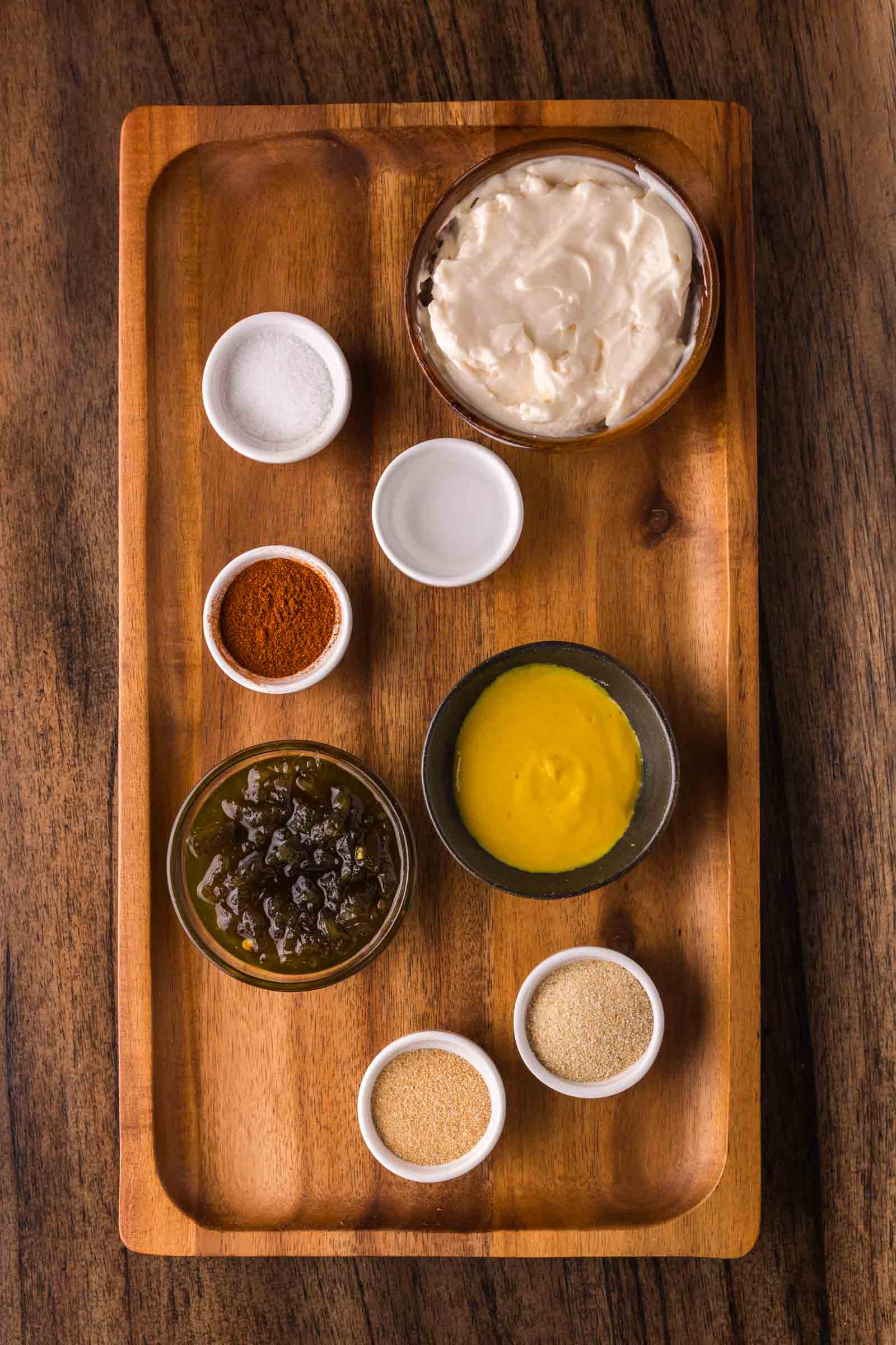 A wooden tray holds small bowls containing mayonnaise, mustard, pickle relish, onion powder, garlic powder, paprika, salt, and vinegar.