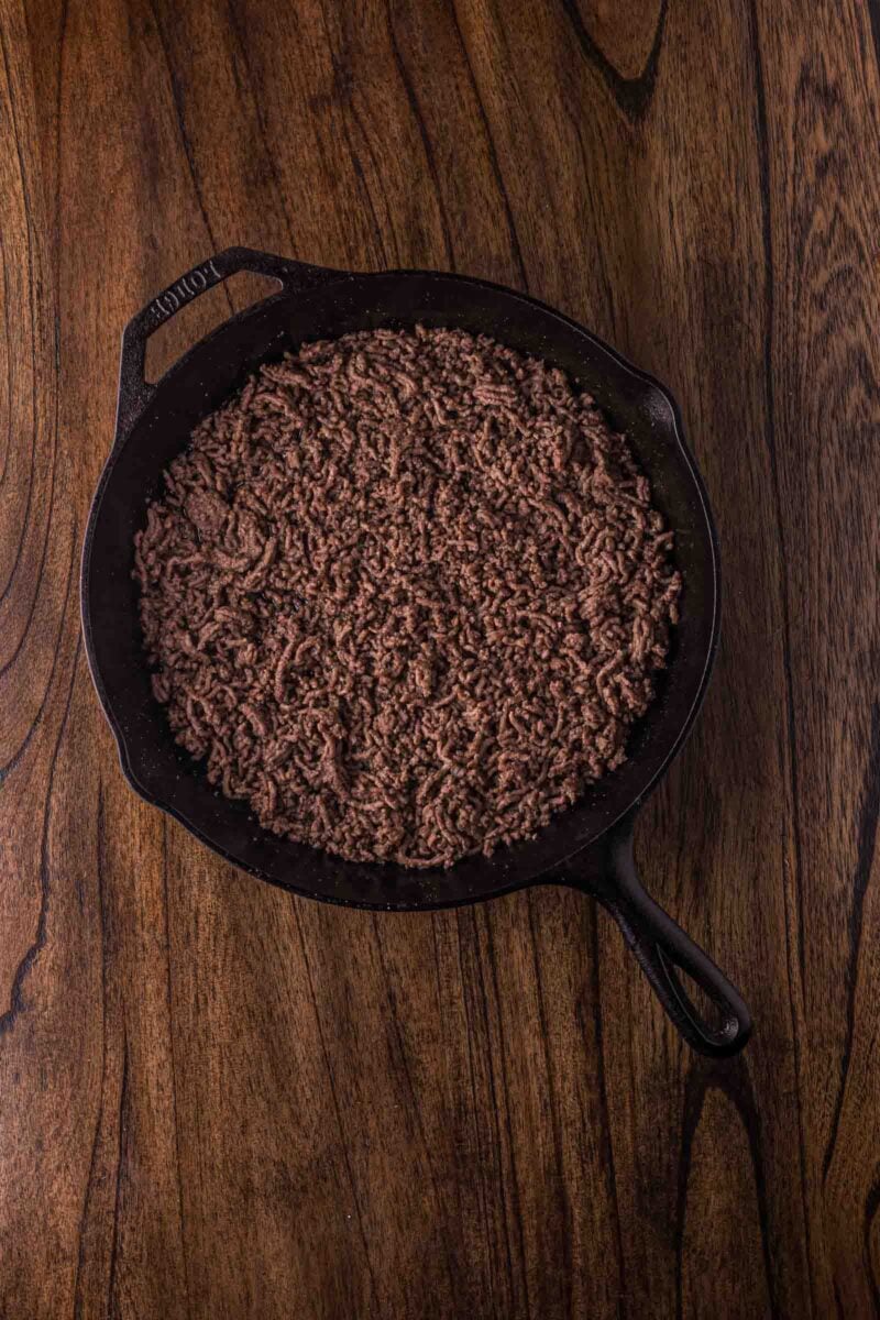 Cooked ground beef in a black cast iron skillet placed on a wooden surface.