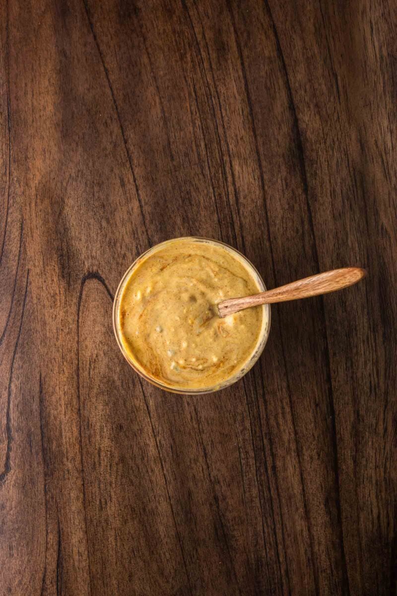 A small bowl of thick, yellowish-brown big mac special sauce with a wooden spoon on a dark wooden surface.