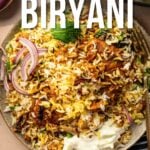 A plate of chicken biryani topped with sliced red onions and herbs, with a striped napkin and fork on the side. Text overlay reads "How to Make Chicken Biryani.