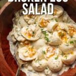 A wooden bowl filled with sliced hard-boiled eggs coated in a creamy dill sauce, garnished with herbs. A spoon rests in the bowl. Text over the image reads "How to Make Creamy Dill Broken Egg Salad.