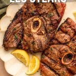Two grilled lamb leg steaks served on a white plate with lemon wedges, garnished with herbs. Recipe information is shown at the bottom of the image.