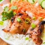 Lemongrass chicken served on white rice with sliced cucumbers, shredded carrots, and cilantro, garnished with chopped green onions.