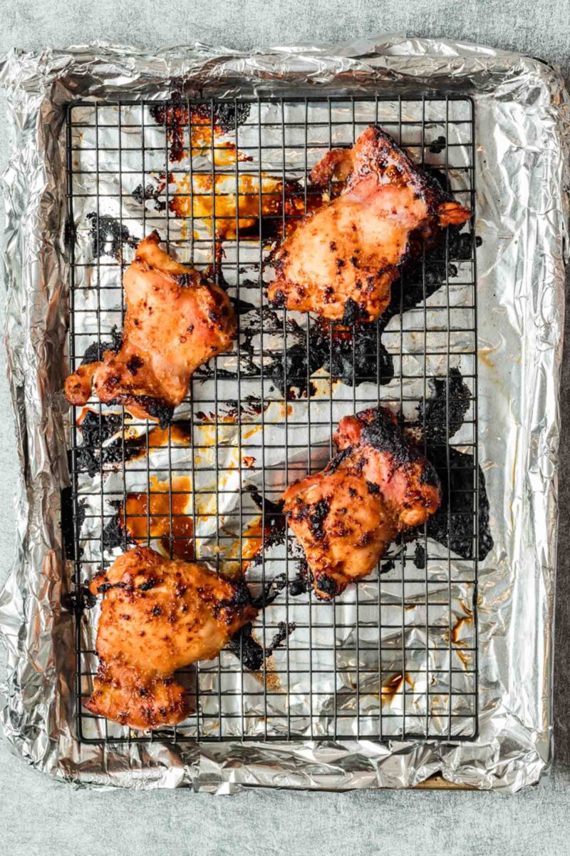 Four cooked lemongrass chicken thighs on a wire rack over a foil-lined baking sheet, with some charred spots and caramelized marinade visible.