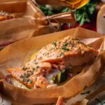 A baked salmon fillet on top of vegetables in a parchment paper boat on a plate, with text promoting a recipe for parchment salmon boats.