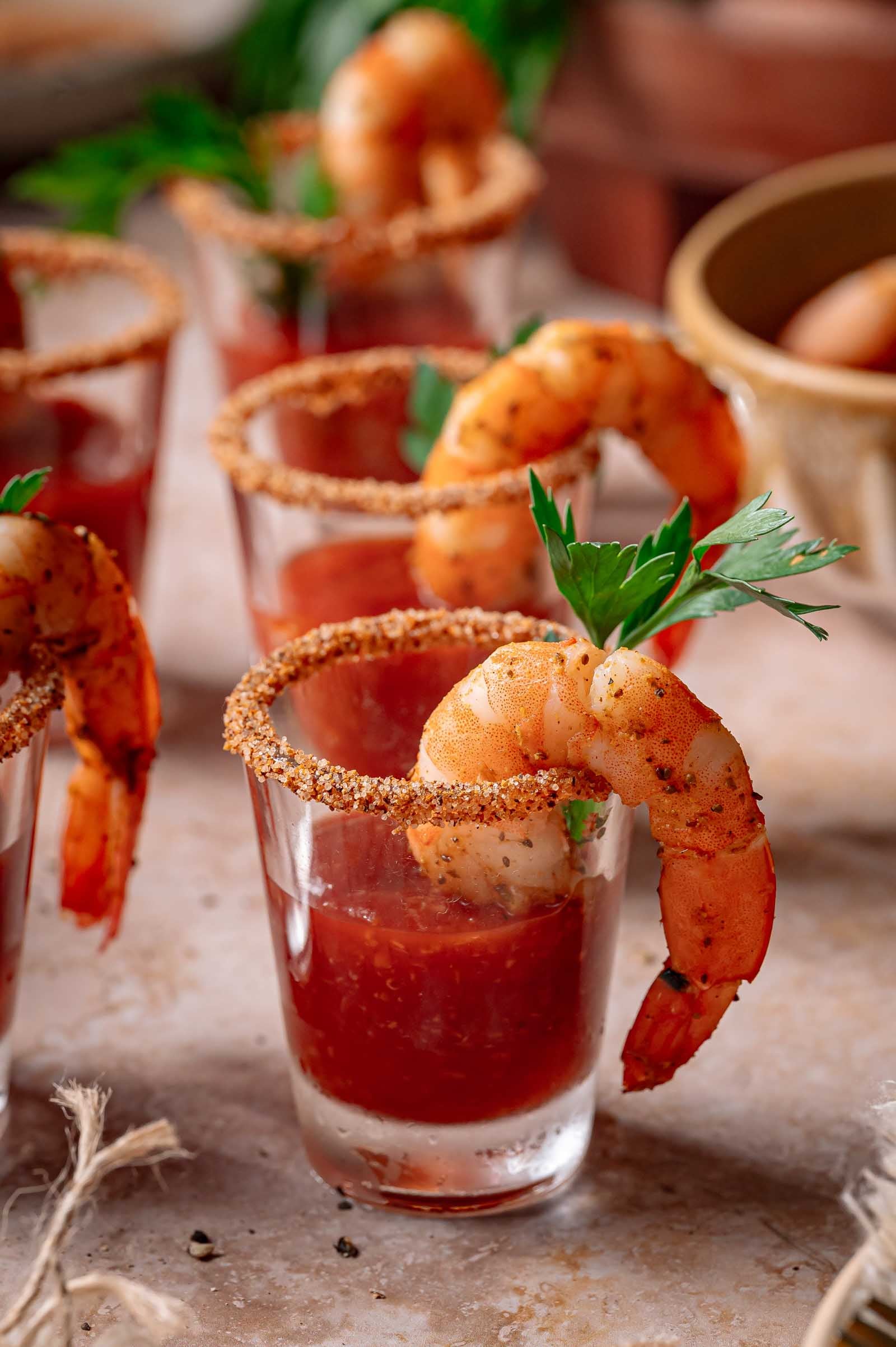 Shrimp cocktail served in shot glasses with seasoned rims, cocktail sauce, and garnished with parsley.