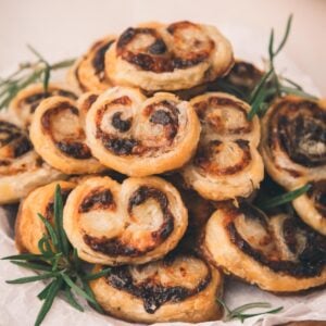 A plate of puff pastry pinwheels with a bacon jam filling, garnished with sprigs of rosemary, arranged on parchment paper.