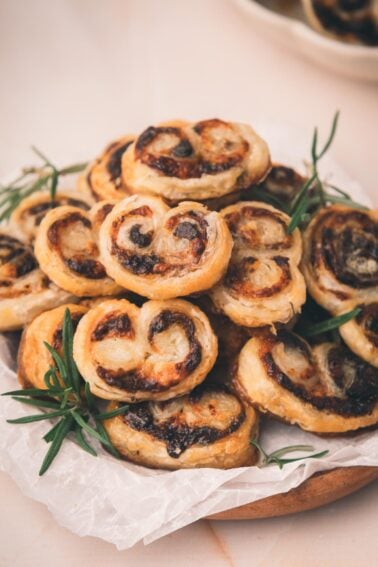 A plate of puff pastry pinwheels with a bacon jam filling, garnished with sprigs of rosemary, arranged on parchment paper.