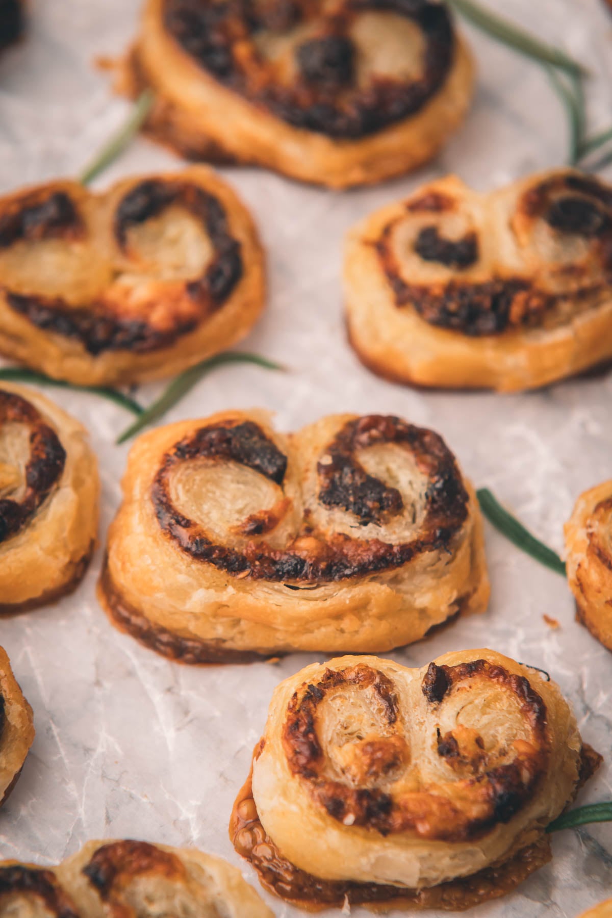 Close-up of several golden-brown bacon jam palmiers with a crispy, flaky texture arranged on a sheet of parchment paper.