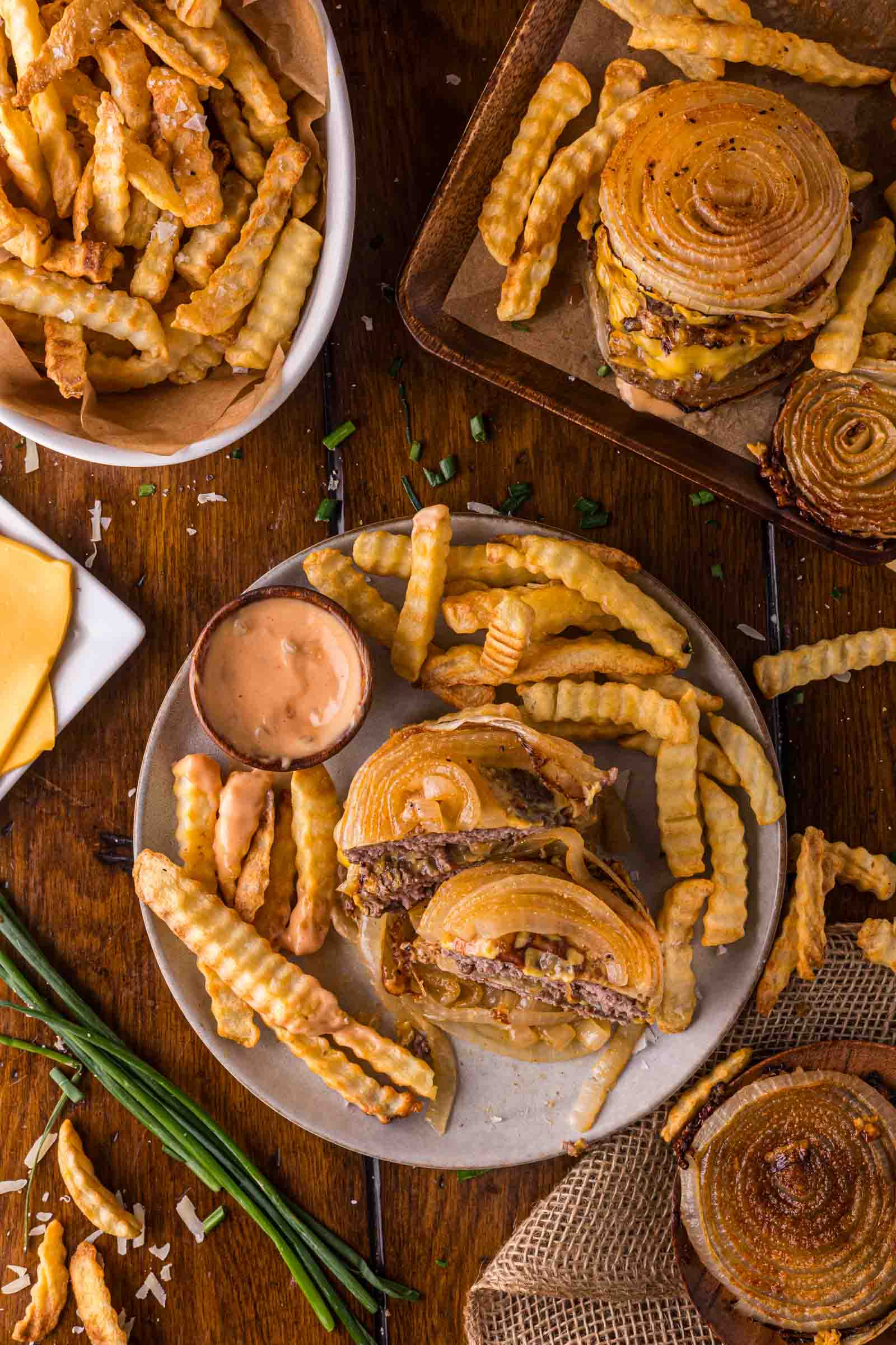Overhead view of crinkle-cut fries and Flying dutchman burgers with large onion slices instead of buns, served with animal sauce on a wooden table.