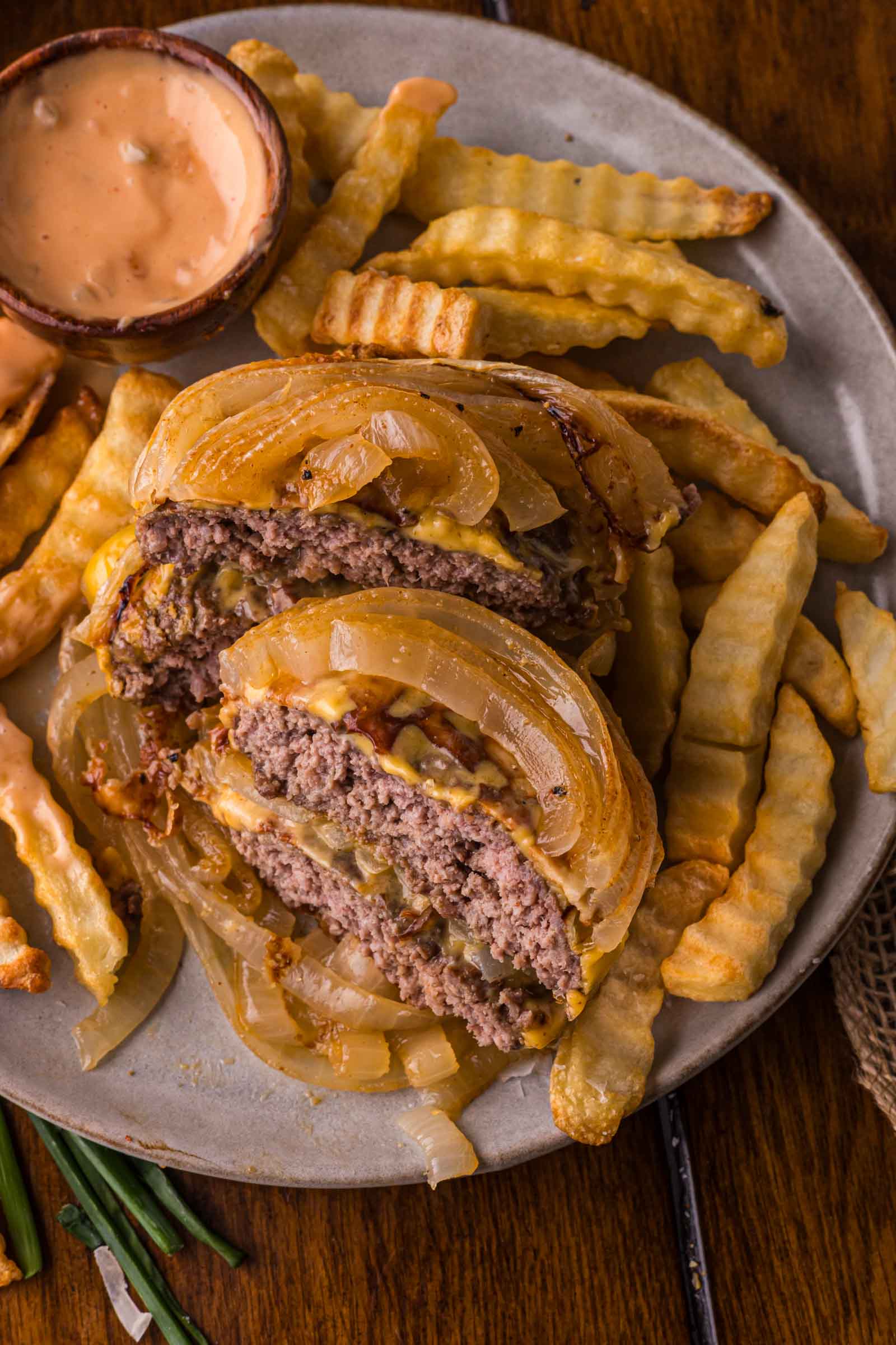 A plate with a bun free sliced flying dutchman burger, crinkle-cut French fries, and a small cup of animal sauce.