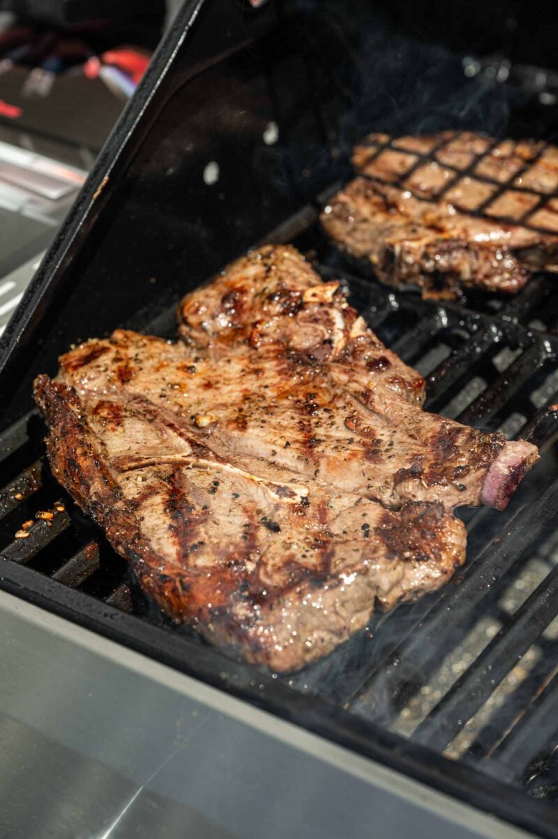 Lamb shoulder chops are cooking on a grill with visible char marks.