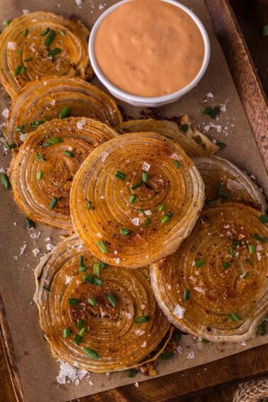 Sliced roasted onion chips garnished with chopped chives and coarse salt, served on parchment paper with a bowl of creamy dipping sauce.