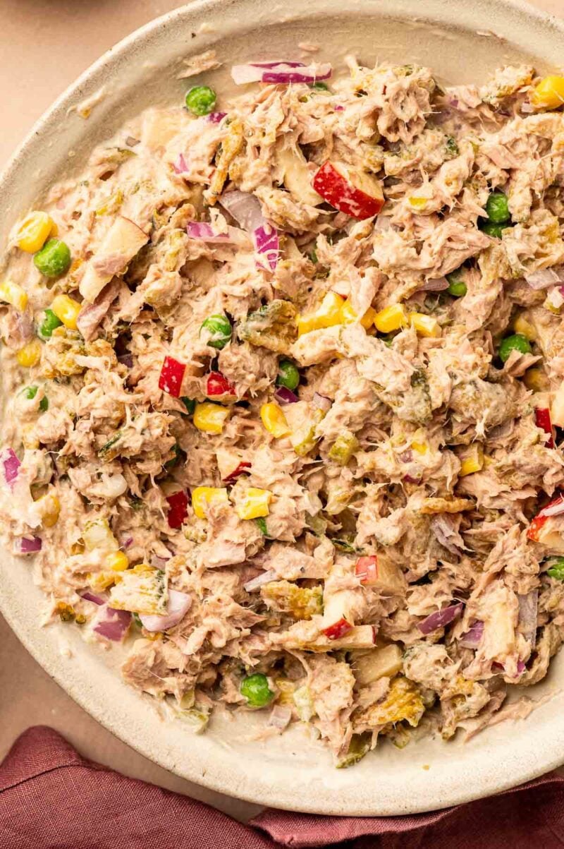 Bowl of tuna salad mixed with chopped onion, peas, corn, apple, and mayonnaise.