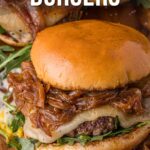 Close-up of a French onion burger with caramelized onions, melted cheese, arugula, and a toasted bun. Text at the top reads “How to Make French Onion Burgers.”.