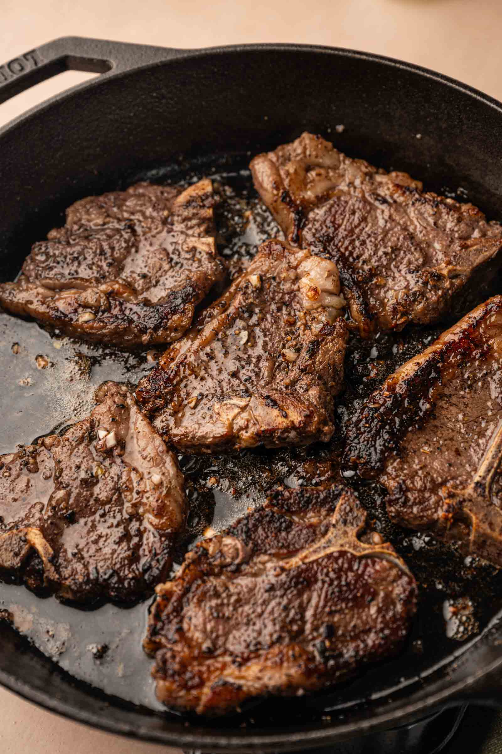 Laamb chops sizzling in a black cast iron skillet, with a seared brown exterior and visible crust.