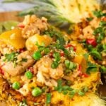 Pineapple chicken and rice served in a halved pineapple, garnished with chopped cilantro, with a lime wedge on the side.