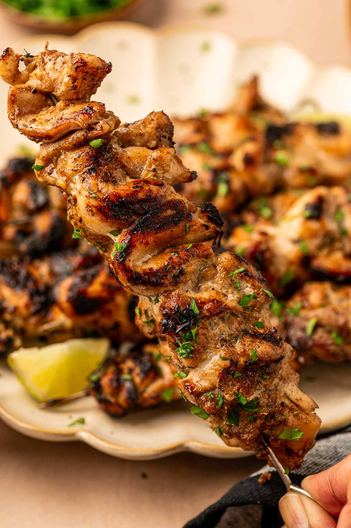 Grilled jerk chicken skewers garnished with herbs are served on a plate with a lemon wedge in the background.