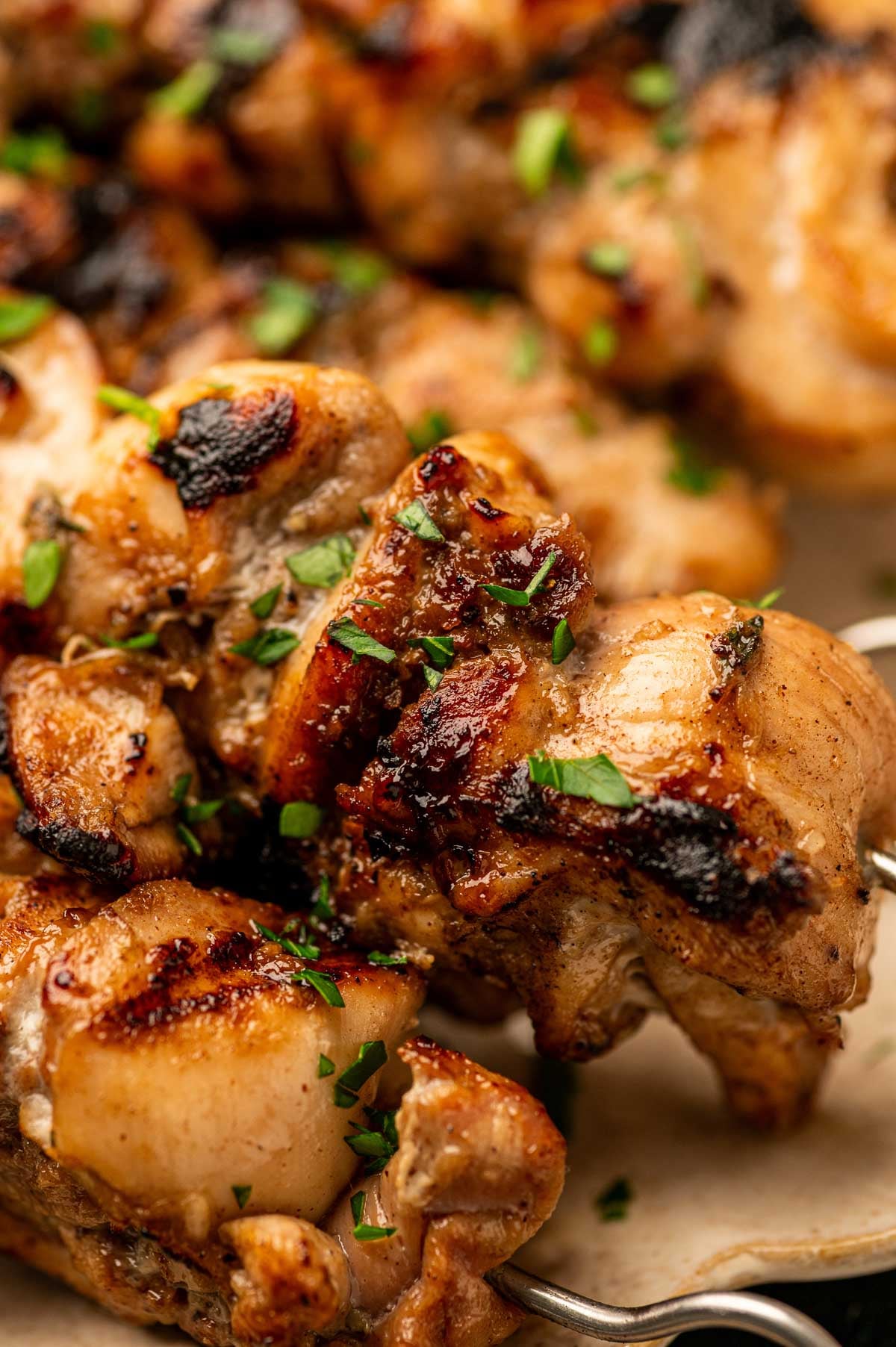 Close-up of grilled jerk chicken pieces on skewers, garnished with chopped fresh herbs.