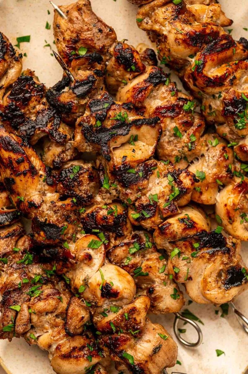 Grilled jerk chicken skewers with a charred exterior, garnished with chopped parsley, arranged closely on a plate.