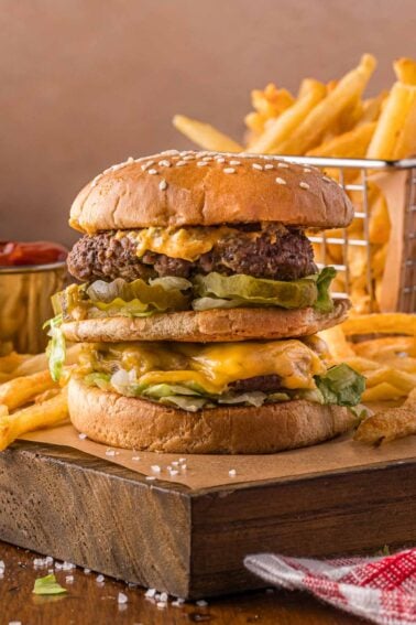 A double cheeseburger with lettuce and sauce on a wooden board, served with a side of French fries and a small container of ketchup.