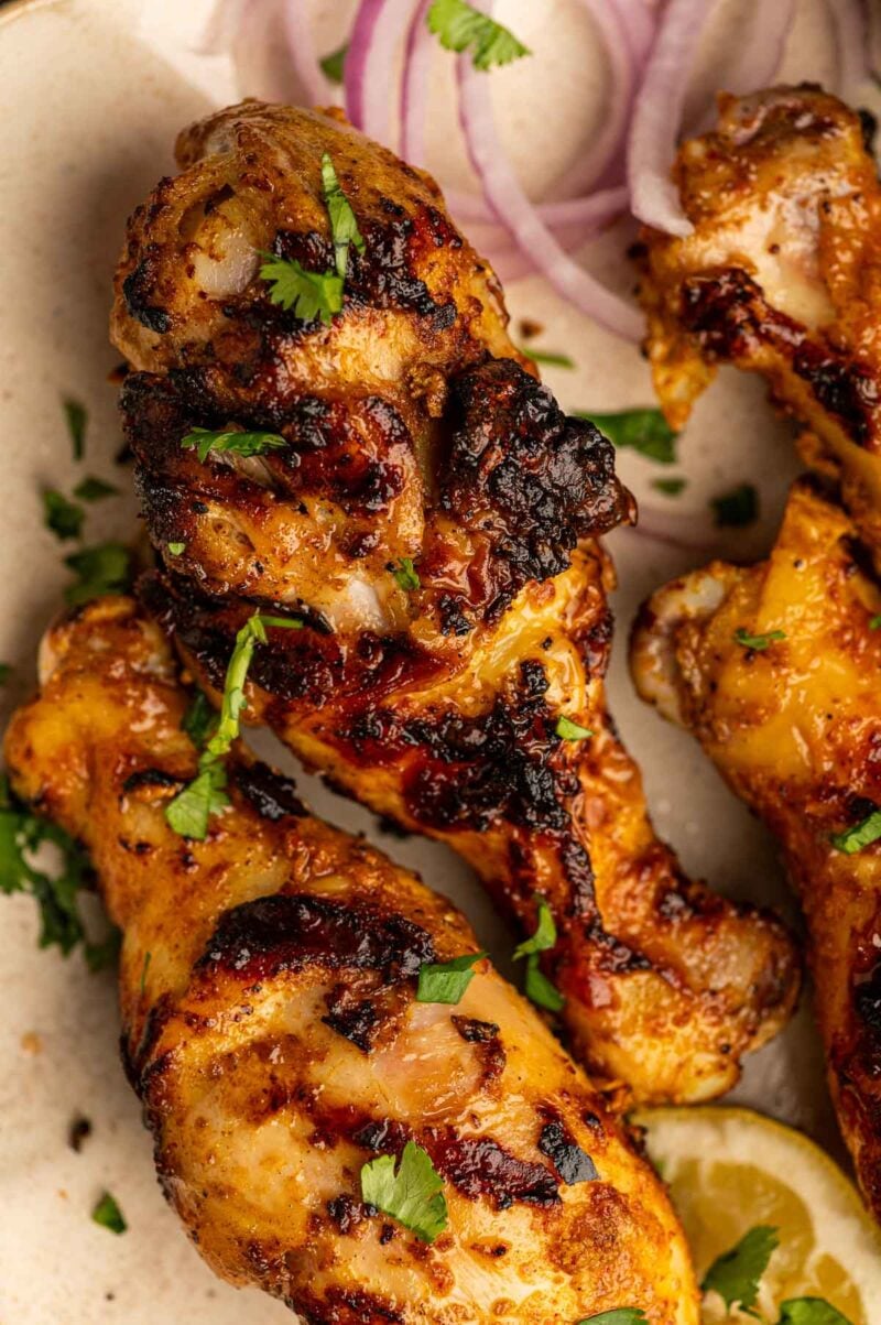 Grilled chicken drumsticks garnished with chopped cilantro, served with sliced red onions and a lemon wedge on a plate.