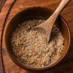 A wooden bowl filled with French onion soup mix, with a wooden spoon resting inside, placed on a wooden surface.