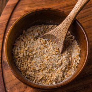 A wooden bowl filled with French onion soup mix, with a wooden spoon resting inside, placed on a wooden surface.