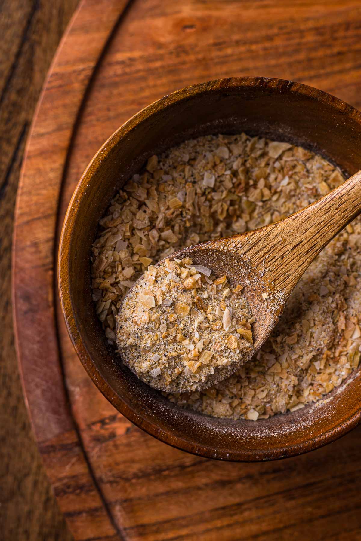 A wooden bowl of french onion soup mix with a wooden spoon resting inside, placed on a wooden surface.