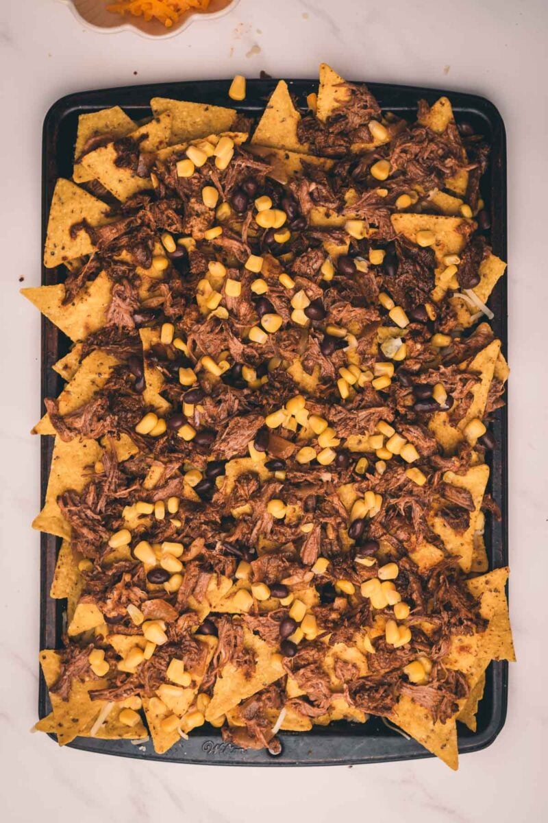 Rectangular tray filled with nachos topped with shredded Mexican beef, corn kernels, and black beans.