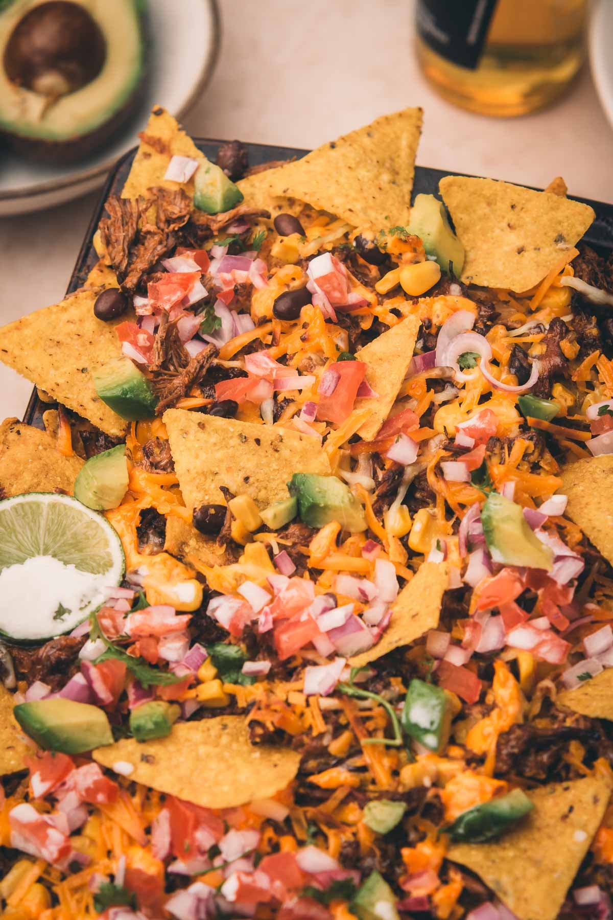 A tray of nachos topped with melted cheese, diced tomatoes, onions, black beans, avocado, and a lime wedge.