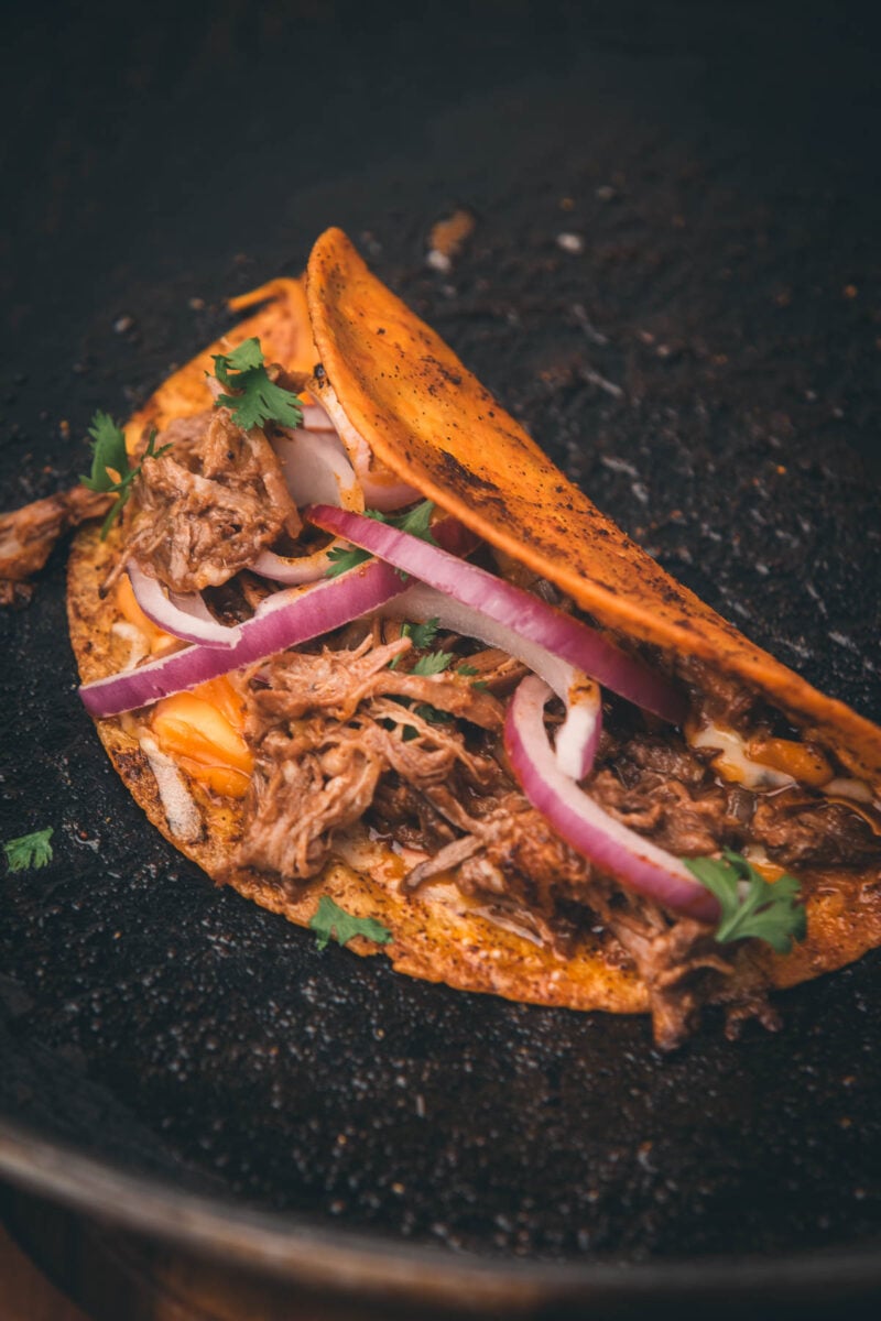 A shredded beef taco with red onions, cilantro, and melted cheese in a skillet.