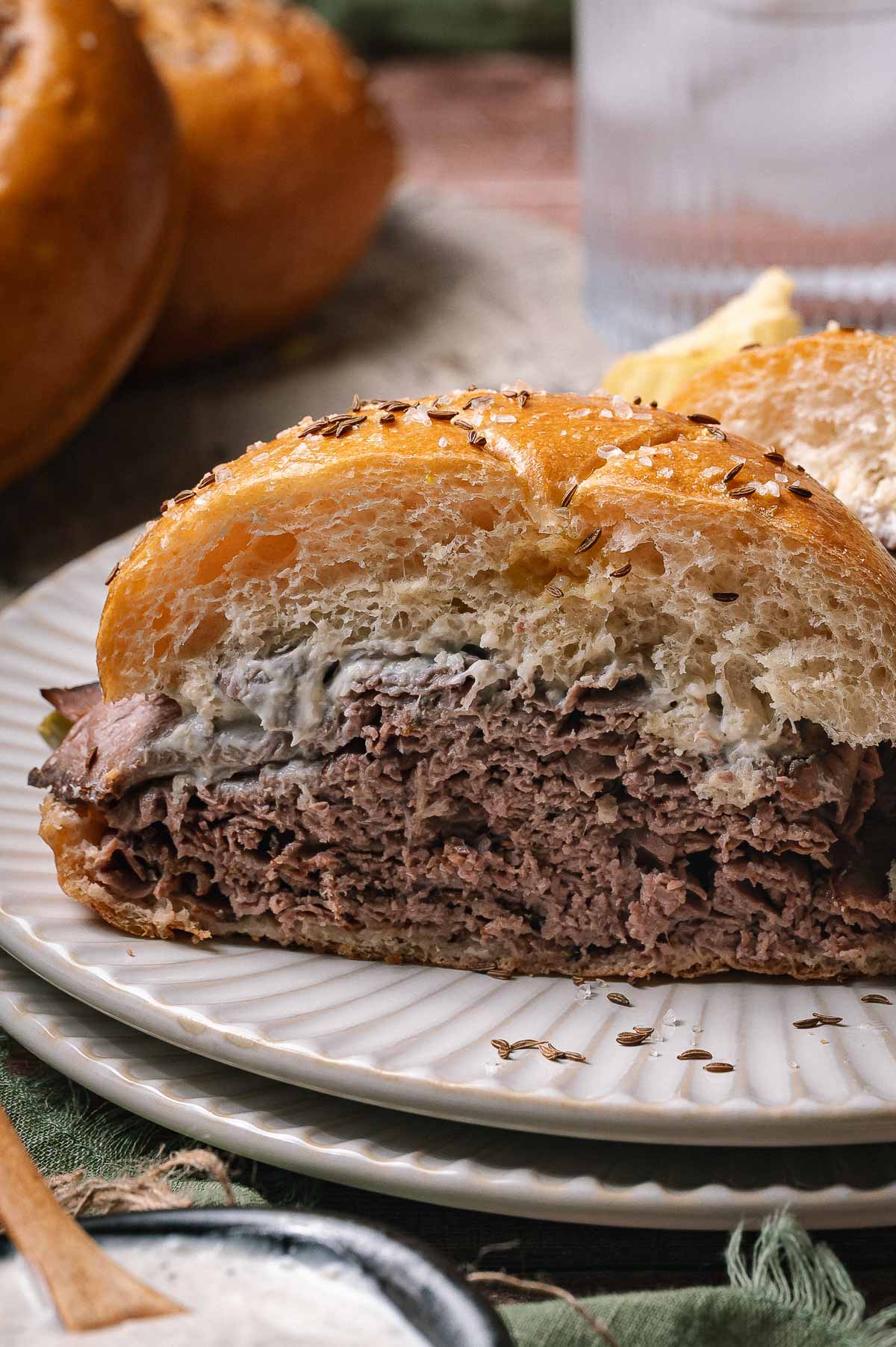 A close-up of a beef on weck sliced down the middle to show a thick layer of sliced beef with creamy sauce on a seeded bun.