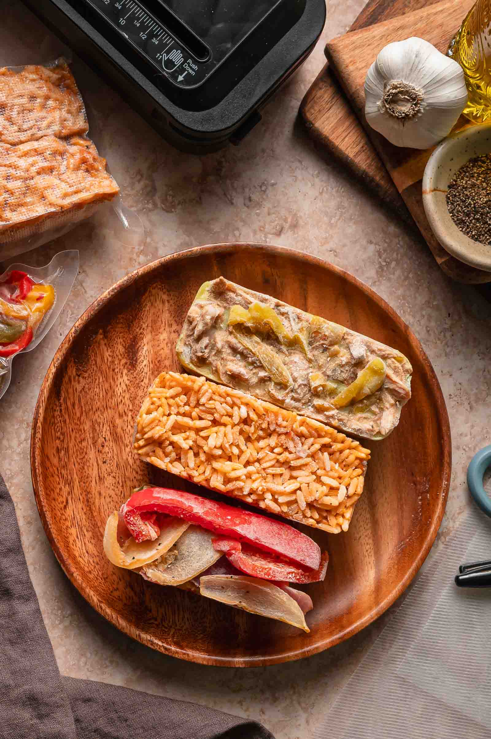 Three rectangular portions of frozen food, including spanish rice and peppers and onions, are arranged on a wooden plate.