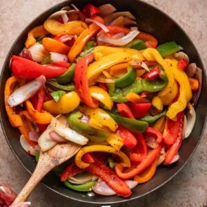 A pan of sautéed bell peppers and onions being stirred with a wooden spoon.
